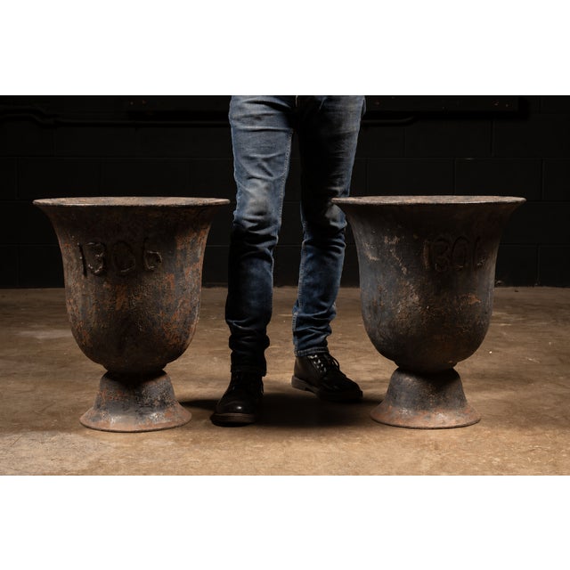 Pair of large cast iron garden urn planters with natural wear that feature welded numbers "1306" on each. These pieces are...