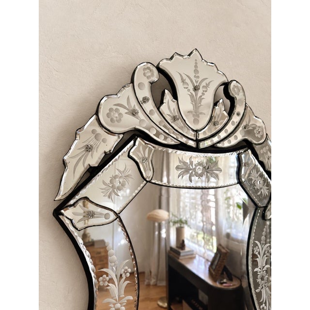 Venetian-style mirror featuring an elaborate sculptural crest, graceful scrolling details, and delicate floral etching...