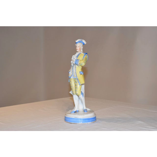 19th century Sitzendorf figure of a gentleman dressed in hand painted finery. He has a blue tricorn hat and a yellow suit,...