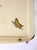 botanical motifs, supported by brass-tone folding legs. The delicate illustration and softly aged finish lend the piece an...