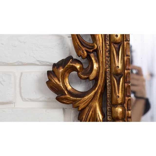 Striking antique wall mirror featuring an elaborate hand-carved giltwood frame with rich openwork detailing. The design is...