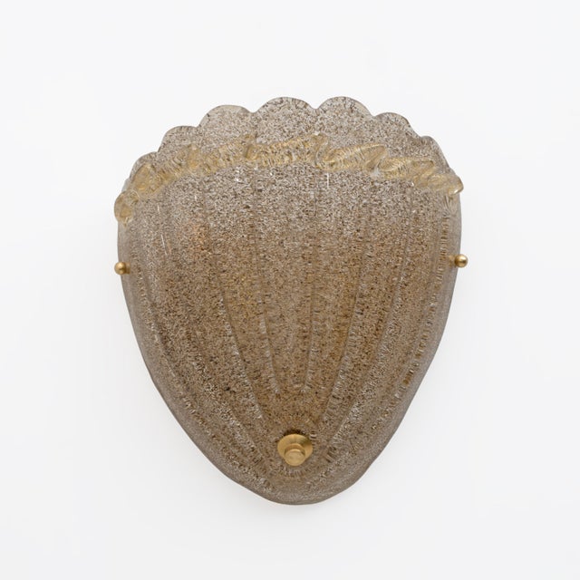 Two Art Deco wall lamps in the shape of a shell. Made of Murano Graniglia glass, mounted on a brass base. The wall lamps...