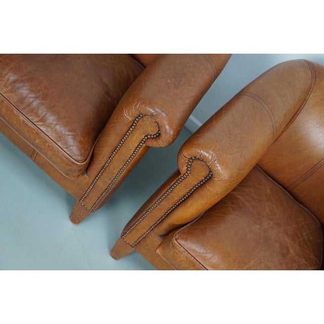 This pair of cognac-colored leather club chairs come from the Netherlands. They are upholstered with cognac-colored...
