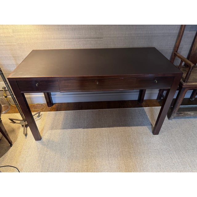 Carlton Desk by Roman Thomas Dark brown walnut desk with * Three dovetailed drawers * Center drawer includes a custom...