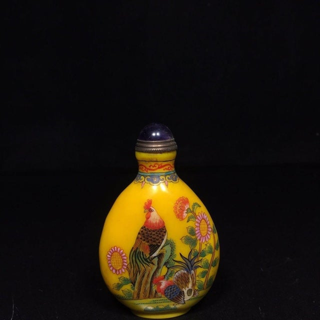 This is a finely crafted antique glass snuff bottle, featuring a hand-painted enamel design on a bright yellow ground. The...