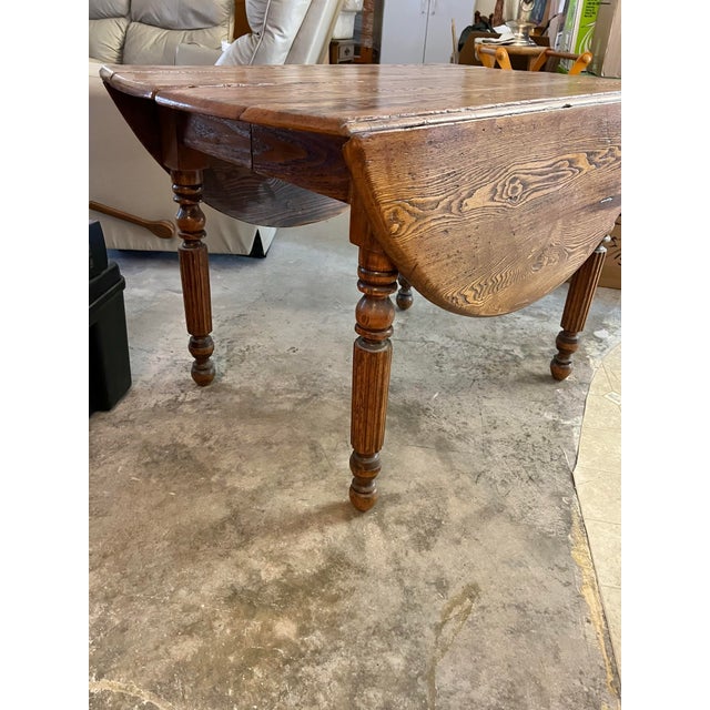 Antique wood drop leaf dining table features turned legs and a distinct grain pattern, resembling farmhouse or Victorian-...