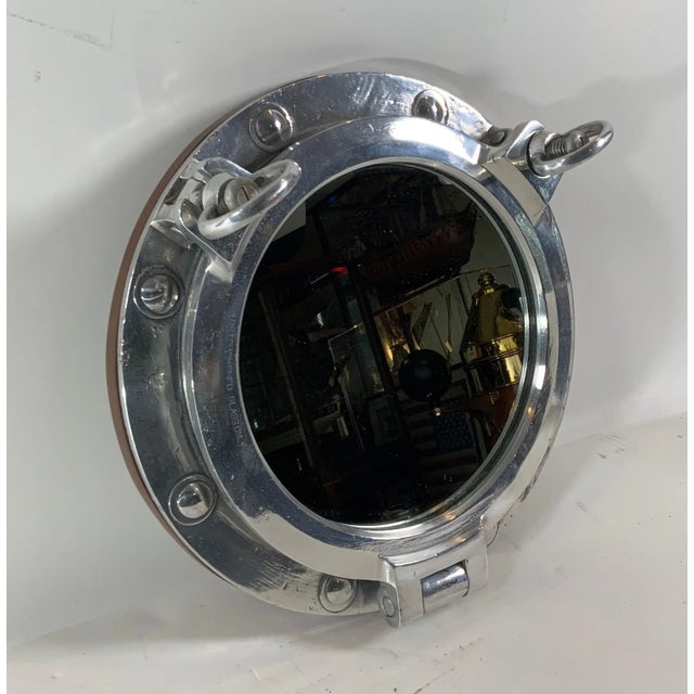 Authentic polished aluminum ship's porthole fitted with a glass mirror. Door is hinged and fitted with two dogbolts. The...
