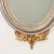 A regal gold and silver gilt mirror with intricate, carved details at the top and bottom. A splendid Ho-oh bird (or...