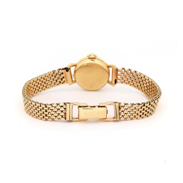 Vintage Omega ladies dress watch in 14K yellow gold featuring a round case with a fluted sunburst bezel, silver-tone Clous...