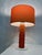 1 table lamp from the 1970s. Orange glass base with white painted metal bottom, orange fabric covered lamp shade. This...