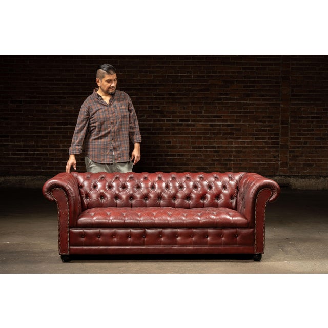 Handsome Chesterfield-style sofa upholstered in richly patinated oxblood-red leather. The substantial frame features a...