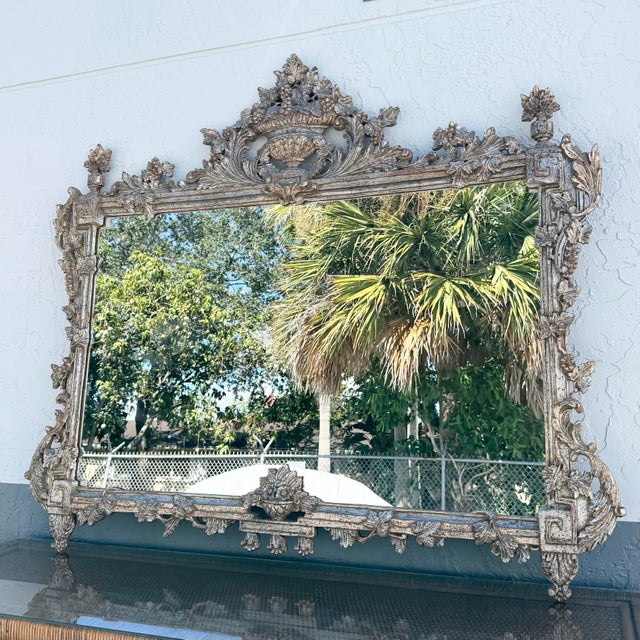 An impressive Italian antique-style Venetian mantel mirror featuring an elaborately carved frame with an aged silver-gilt...