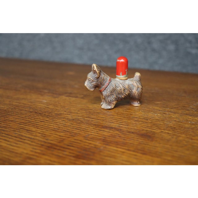 Figural table lighter depicting a standing Scottish Terrier with a textured coat, red collar, and upright ears. The brown...
