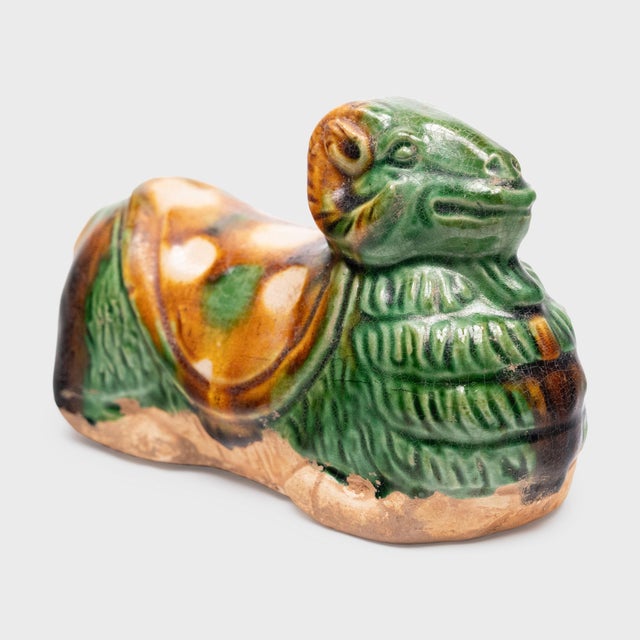 This petite ceramic figurine from the early 20th century fits in the palm of the hand, sculpted as a recumbent ram with...