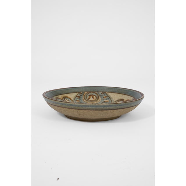 A decorative stoneware bowl by Søholm featuring expressive hand-painted motifs in earthy blue and brown tones. The...