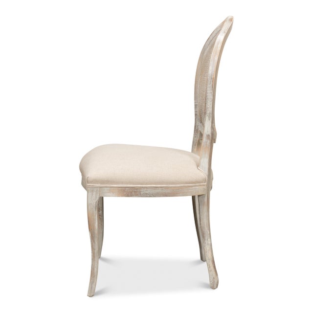 An oval of woven cane sits within each carved back, painted to match the frame so the weave reads as texture rather than...