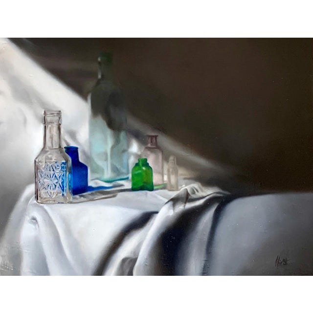 This oil on panel work features a serene arrangement of glass bottles, each reflecting light in a unique way against a...