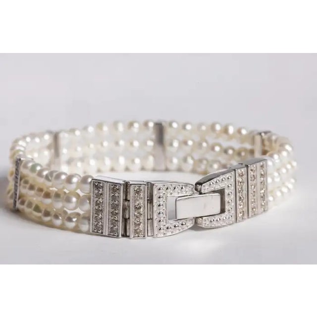 A three strand beaded pearl bracelet with 4 diamond bars between the pearls and a sterling silver and diamond snap-shut...