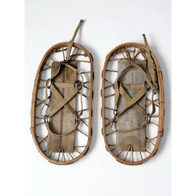 Pair of vintage 1940s snowshoes featuring a classic bear claw–shaped wood frame with hand-laced rope webbing and canvas...
