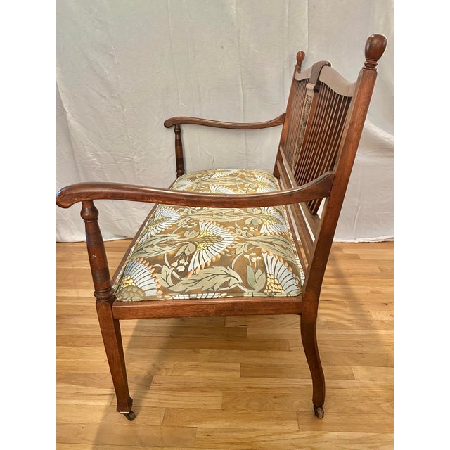 This antique Sheraton Revival settee dates to circa 1890–1905, featuring an unusually graceful spindle back, carved...