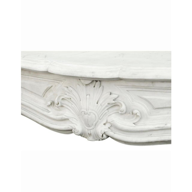 A stunning antique French Louis XV-style fireplace mantel crafted entirely of white marble with elegant gray veining....