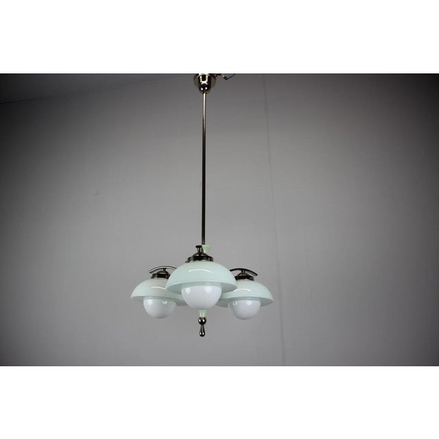 Art Deco chandelier produced in Czechoslovakia during the 1930s. The fixture features three green-white glass shades with...