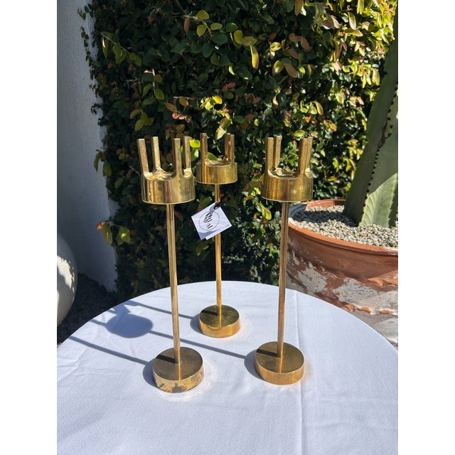 Vintage mid-century trio of solid brass candlesticks featuring a clean, architectural silhouette with cylindrical stems...