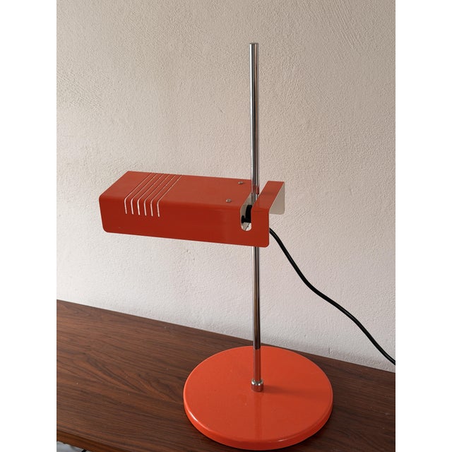 A distinctive space-age desk lamp, likely from the 1970s. It features a rectangular, slotted metal shade, a slender chrome...