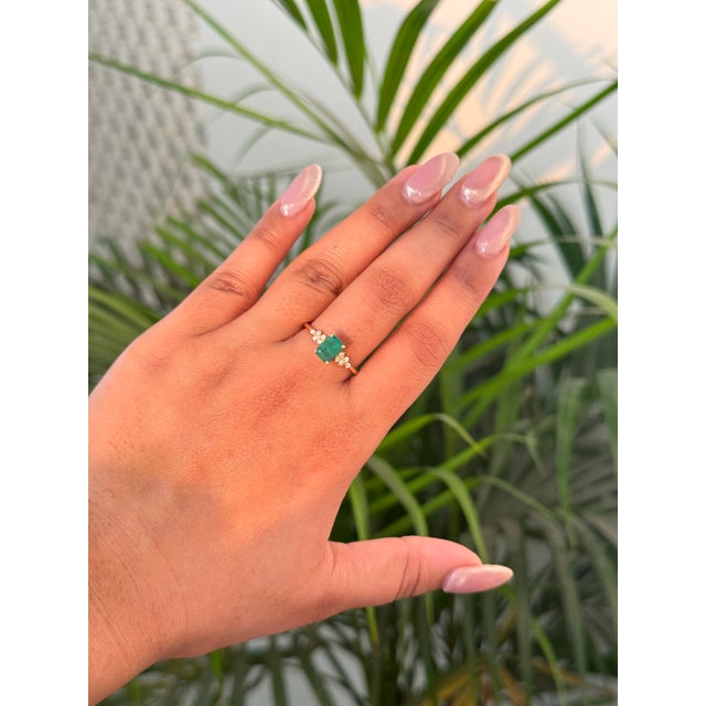 This elegant floral cluster engagement ring features a 1.06 carat emerald-cut natural emerald, securely set in a classic...