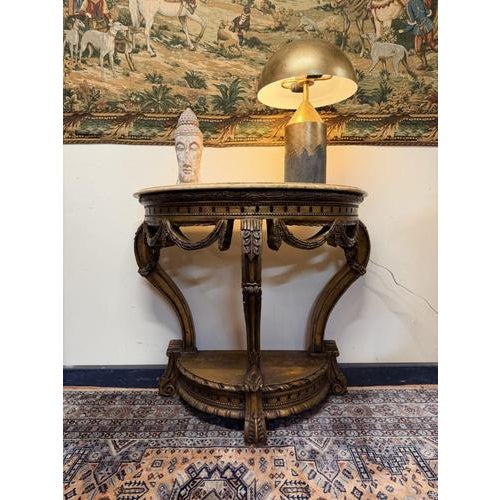 Elegant 20th-century giltwood demilune console table featuring a shaped marble top and beautifully carved decorative...