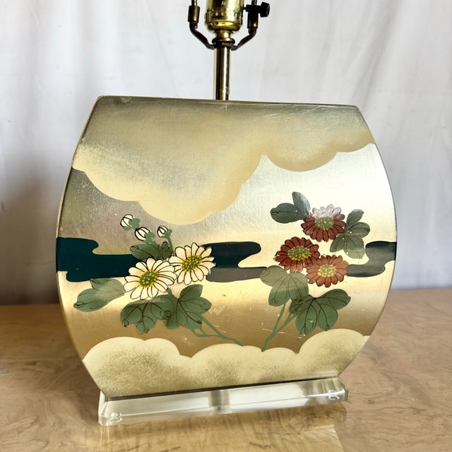 A graceful Chinoiserie table lamp featuring hand-painted florals drifting across soft gold clouds. Its curved silhouette...