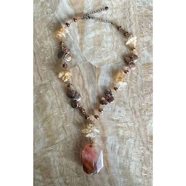 This vintage necklace is an earthy, hand-strung composition that centers on a bold, faceted rectangular pendant in blush...