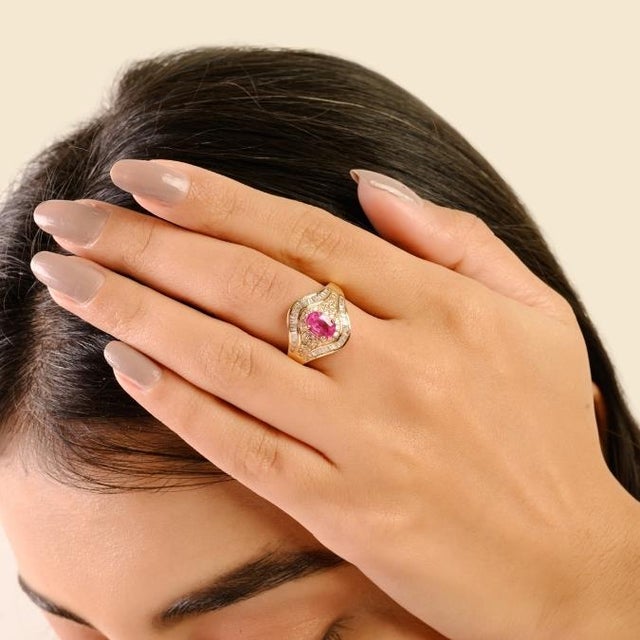 This elegant ring showcases an oval-cut ruby weighing 1 carat, surrounded by brilliant round and baguette-cut diamonds...