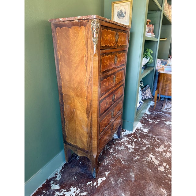 This antique Italian chest features six drawers with intricate floral marquetry, carved accents, brass detailing, and a...