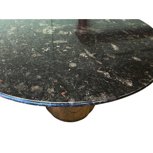 USA, 1970s Round black granite or stone top dining table with a bullnosed edge, resting on a cylindrical brass weighted...
