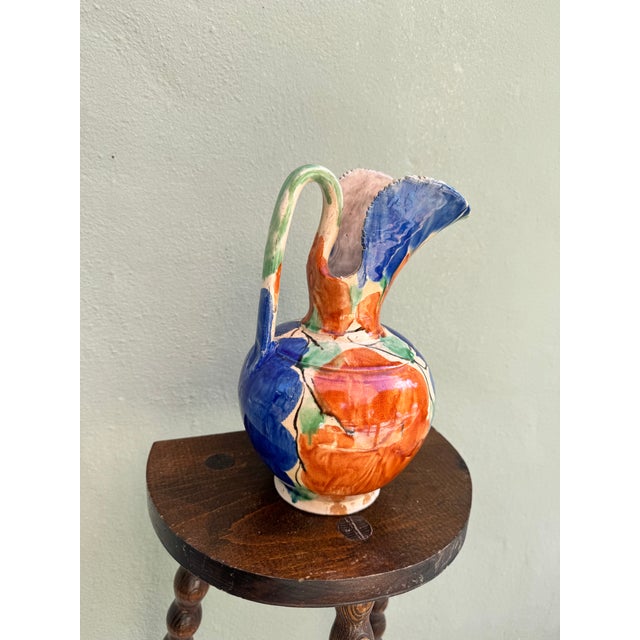 A boldly expressive hand-painted ceramic ewer with a rounded bulbous body, dramatically ruffled and fluted spout, and an...