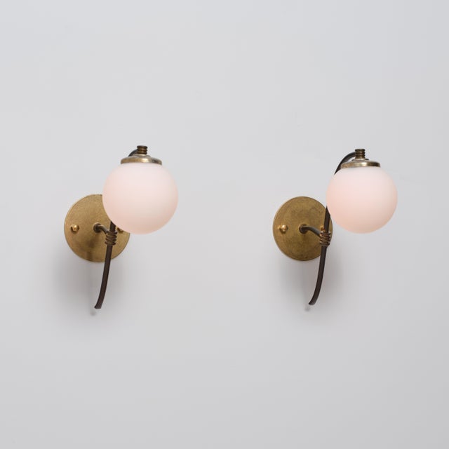 Pair of italian wall sconces from the 1950s, combining a sculptural brass structure with spherical opaline glass diffusers...