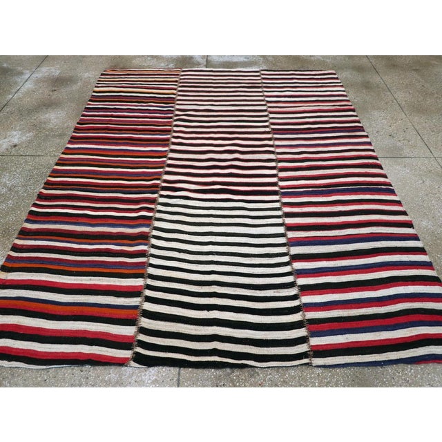This Mid-20th century Persian Flatweave Kilim rug, displays a bold and lively striped design that captures the energy and...