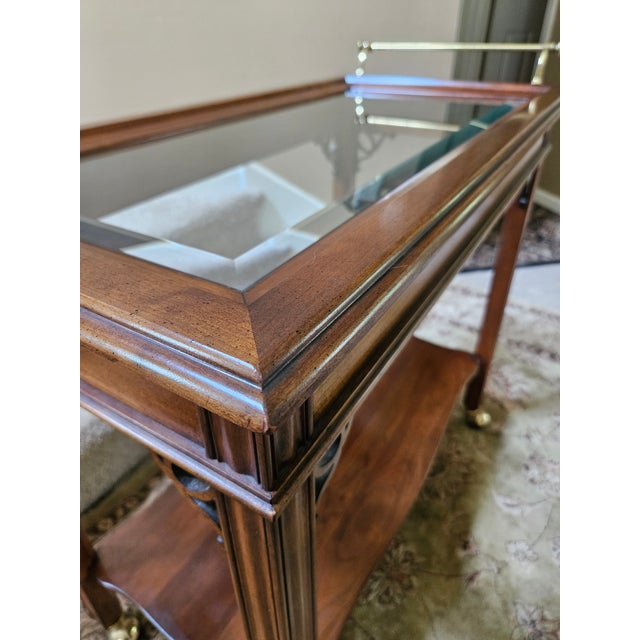 A very well crafted medium toned mahogany rolling bar cart with polished brass push handle and beveled glass insert. There...