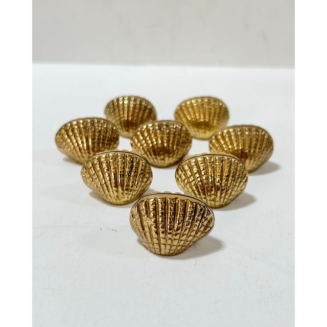 Set of eight vintage solid brass place card holders shaped like scallop shells. Each features a textured shell design with...