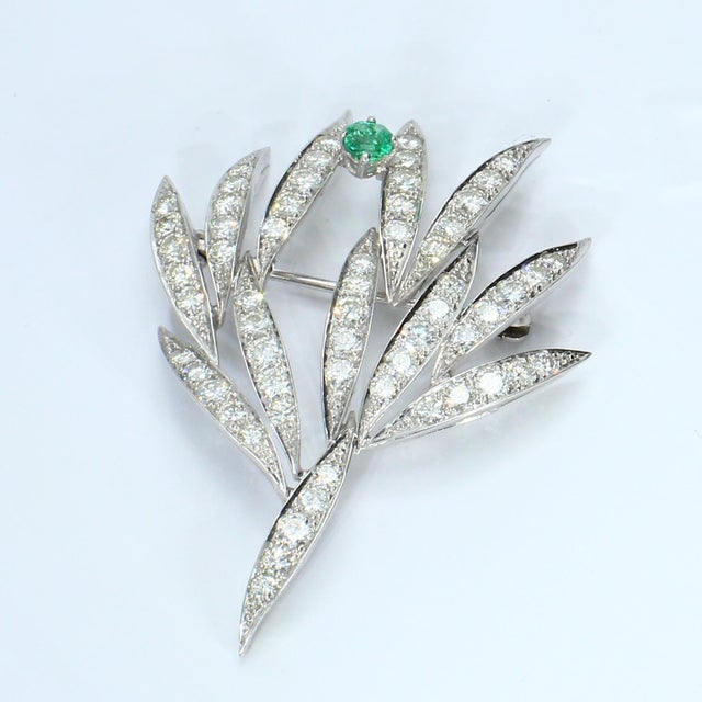 This brooch features a leaf design adorned with a single square-cut green emerald and multiple round white diamonds. Stone...