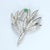 This brooch features a leaf design adorned with a single square-cut green emerald and multiple round white diamonds. Stone...