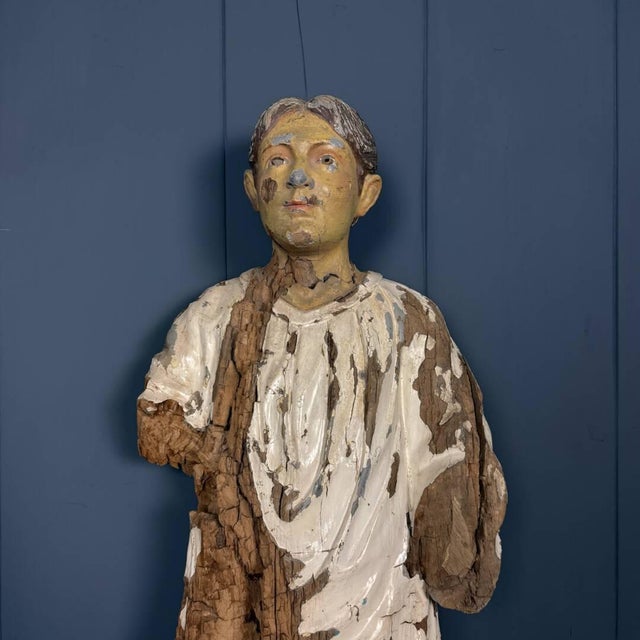 An old, worn wooden statue of a young man. This statue was likely used outdoors for some kind of attraction. Over the...
