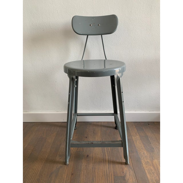 A vintage industrial drafting stool with a round seat, tilt-back, and glossy gray surface.