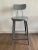 A vintage industrial drafting stool with a round seat, tilt-back, and glossy gray surface.