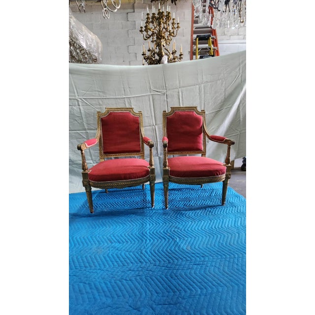 This listing features a pair of red giltwood Louis XVI style pair of chairs, likely originated from France circa 20th...