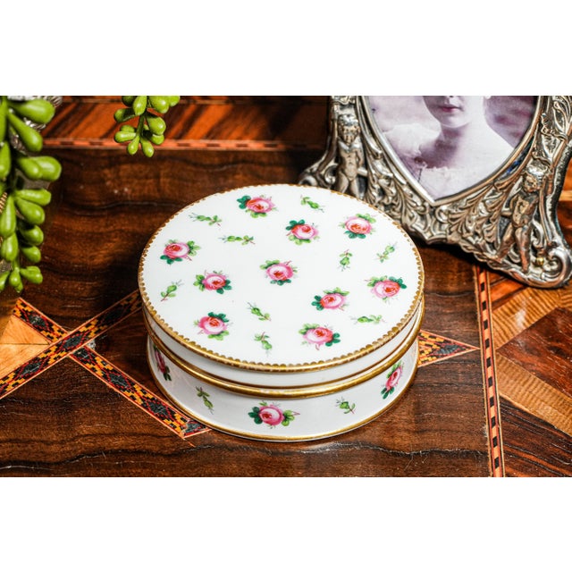 A beautifully refined example of English porcelain artistry, this stunning circular white porcelain box is adorned with a...
