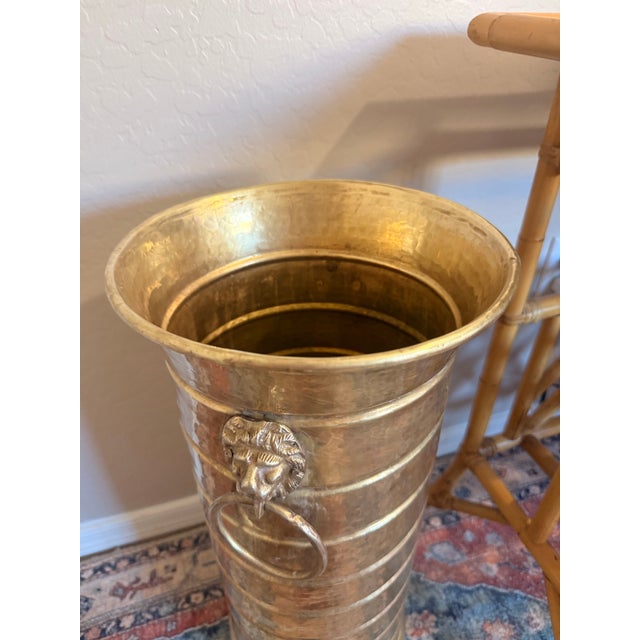 A handsome vintage hammered brass umbrella stand featuring classic lion head ring handles and a beautifully aged brass...