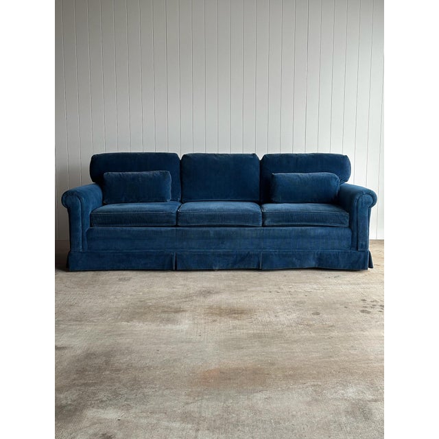 Vintage three-seat sofa upholstered in rich blue corduroy, with rolled arms, a tailored skirt, and a long, low profile....