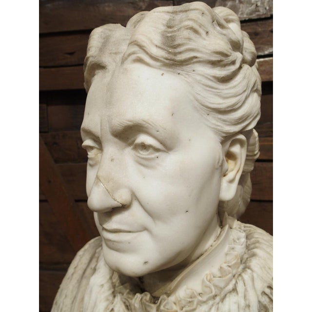 This marble bust of a woman was hand-carved in marble that has a stark white hue with some areas of gray patination. The...